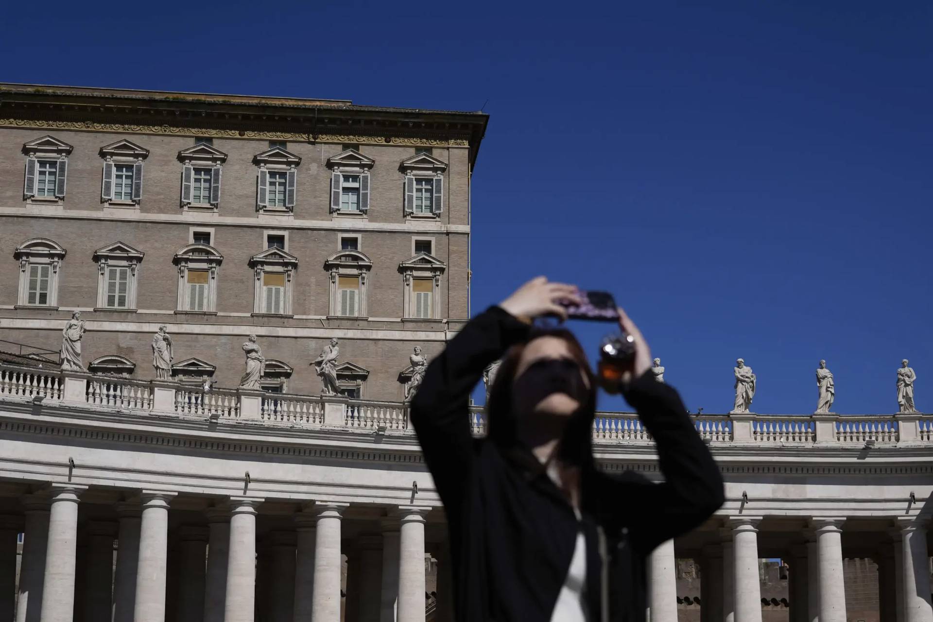 A woman takes pictures in front of the Vatican's Apostolic Palace, where the pope usually delivers his noontime Angelus prayer from the window of his private studio on Sunday, March 30, 2025. (Credit: Gregorio Borgia/AP.)